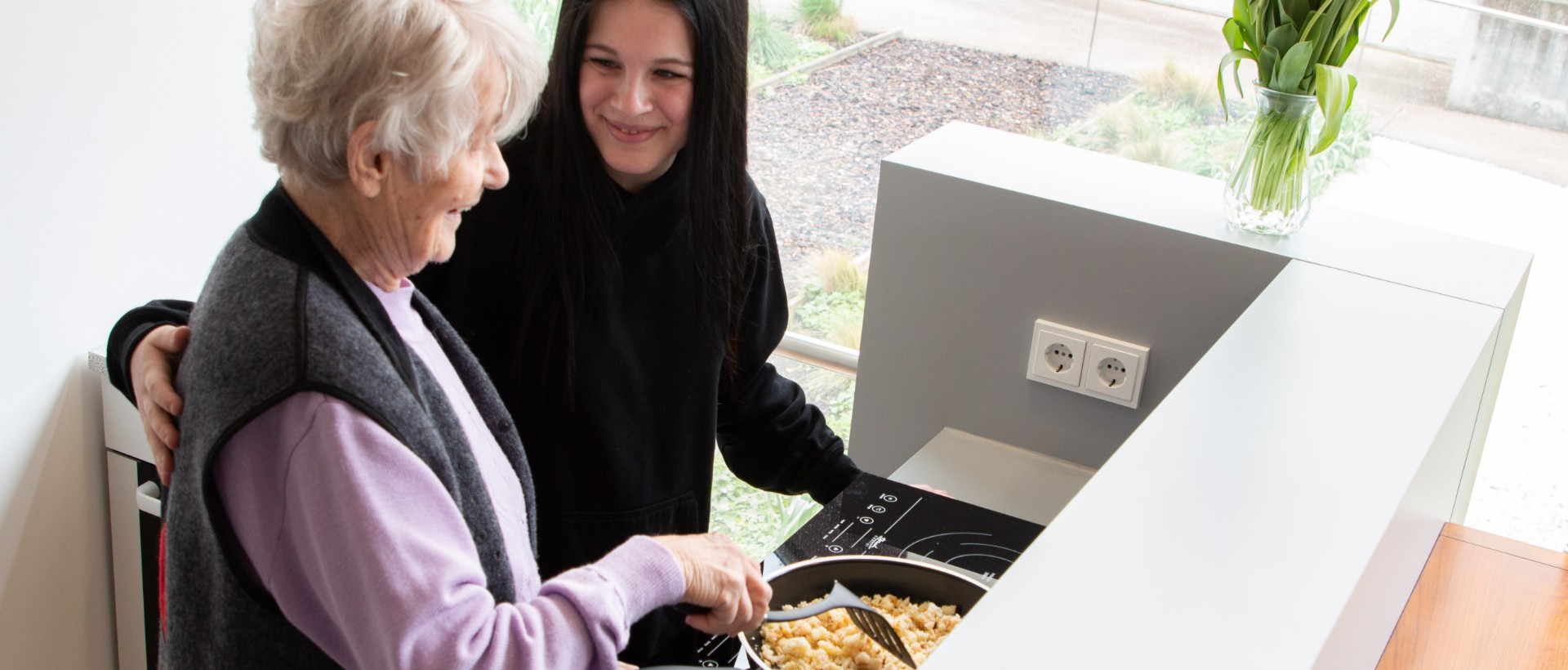 Mädchen hilft älteren Frau beim Kochen im Seniorenhaus